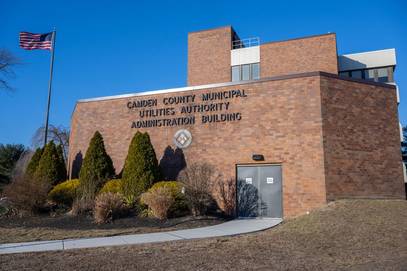 Front of Camden County Municipal Utilities Authority Administration Building with logo, American flag, and landscaped entrance.